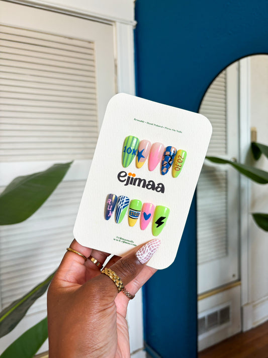 Hand holding a ejimaa nail card with colorful designs. These designs are marathon and race day specific with track and field elements and 'Ejimaa' branding against a blue background.