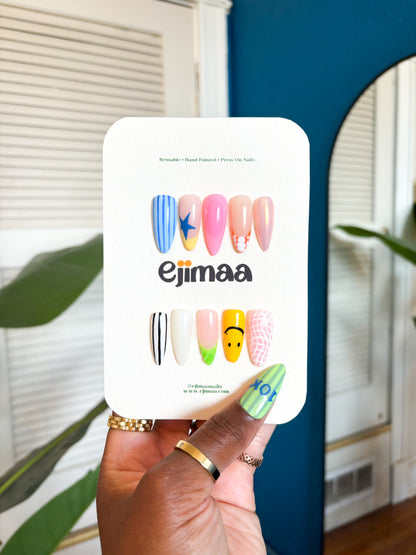 Hand holding a nail art guide with colorful nail designs and 'Ejimaa' branding.