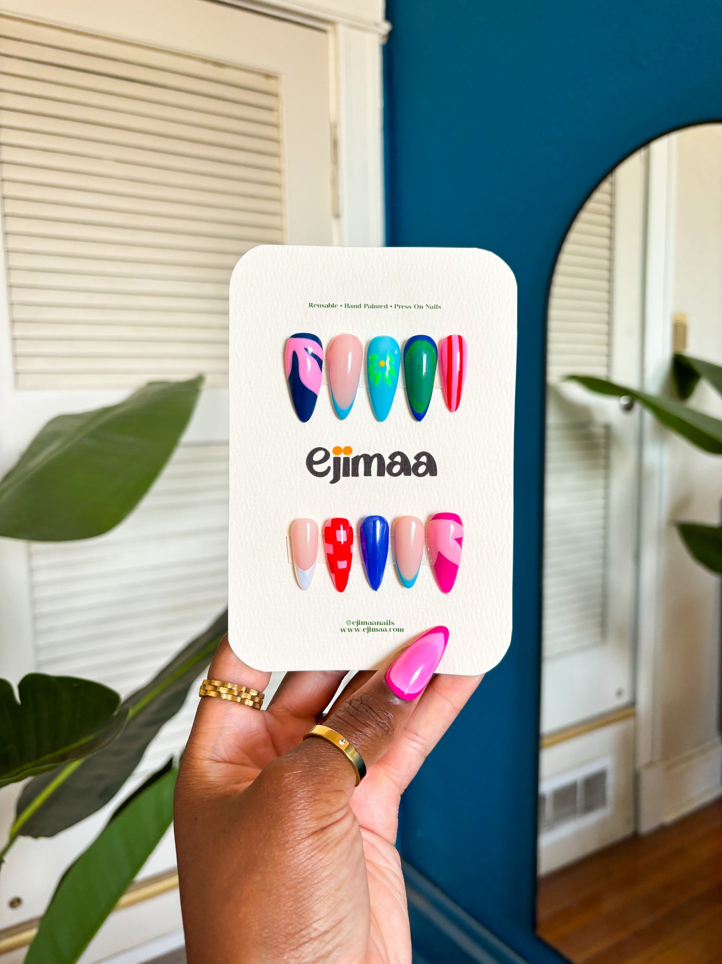 Hand holding a nail card of colorful press-on nails with 'ejimaa' branding. bright summer colors and floral inspirations.