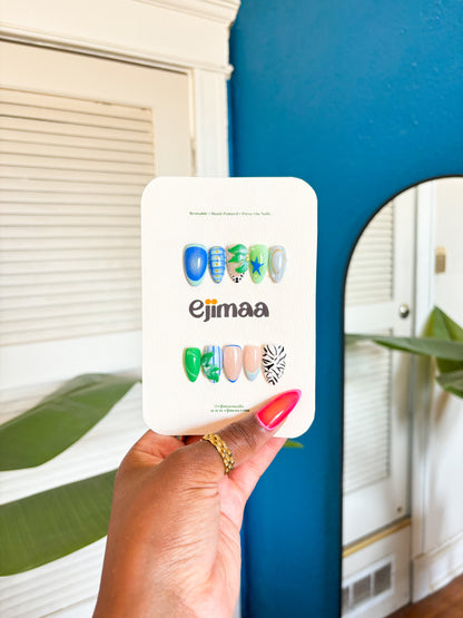 Hand holding a press-on nail product packaging with 'Ejimaa' branding against a blue wall.