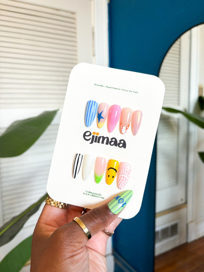 Hand holding a nail art design card with colorful nail designs and 'ejimaa' branding.