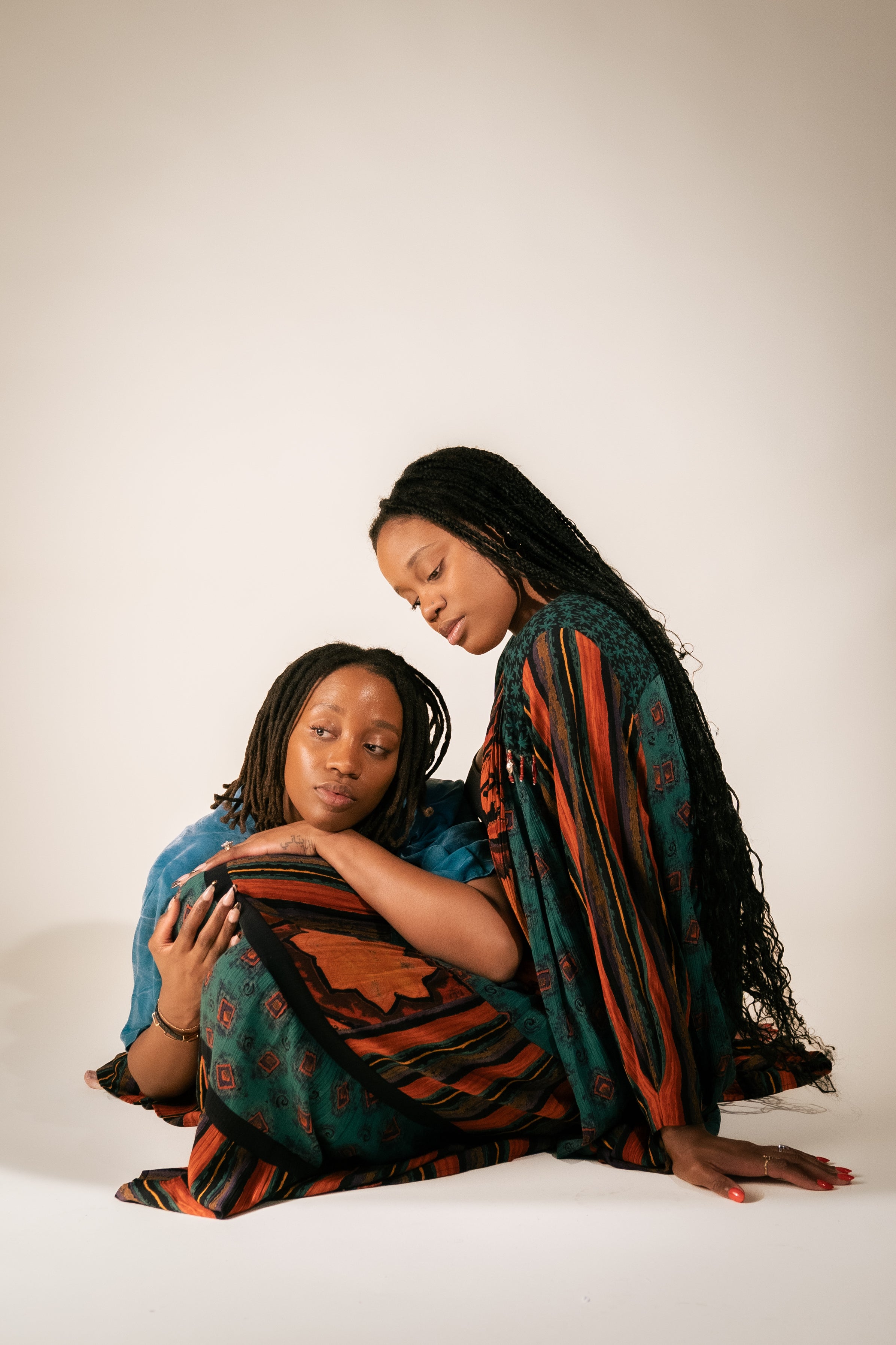 Twin sisters, britny Alexander and Tiffany Alexander Dawkins sitting together wearing patterned clothing on a plain background