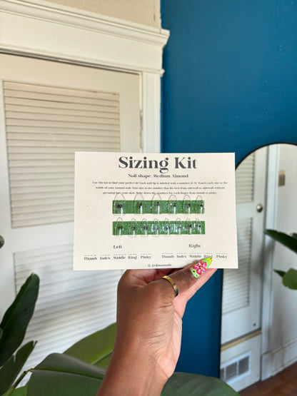 Hand holding a 'Sizing Kit' card with measurement chart against a blue wall.