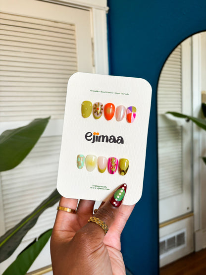 Hand holding a card with colorful nail designs and 'ejimaa' branding.