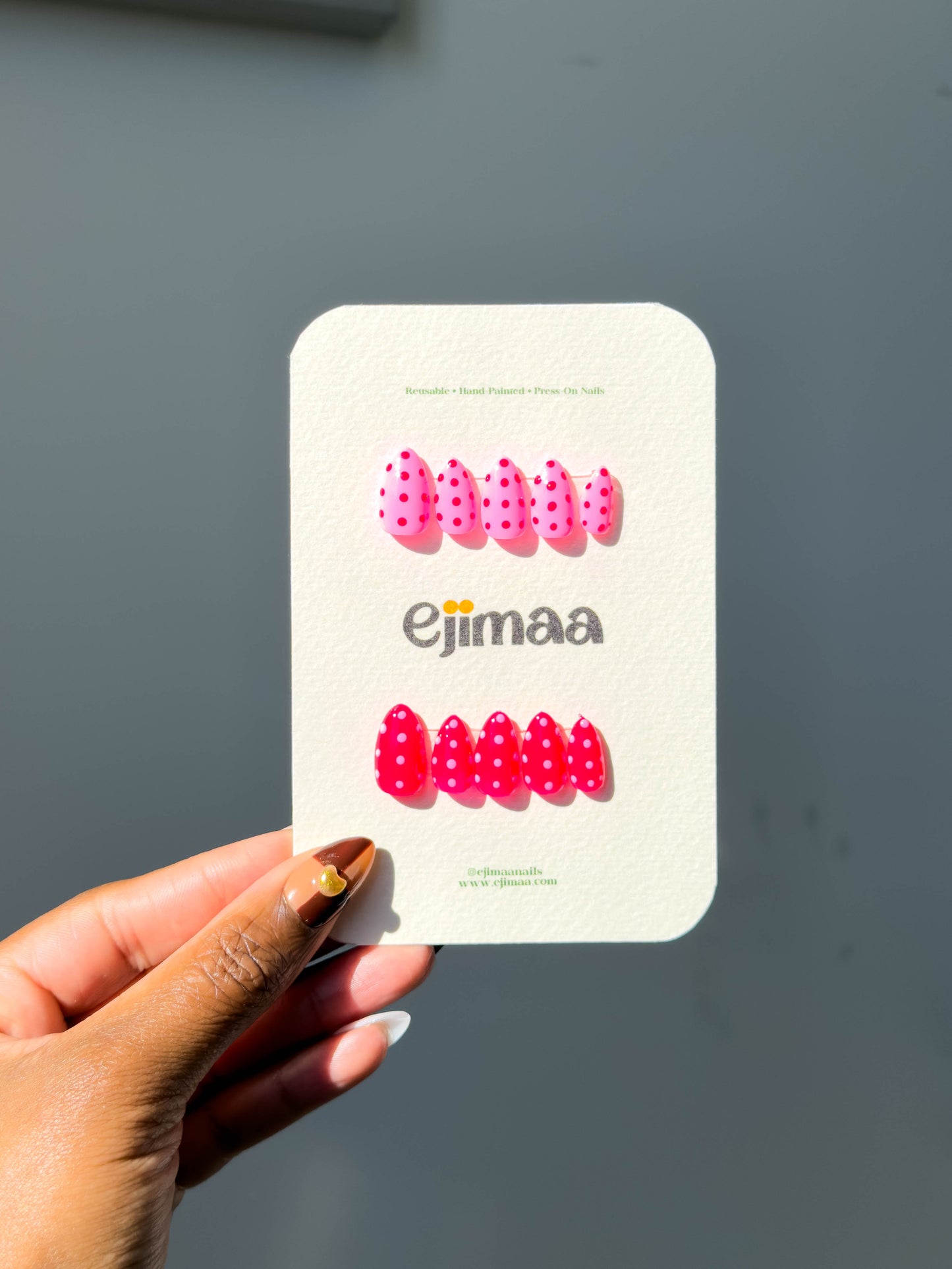 Hand holding a nail cared with 'Ejimaa' branding against a gray background