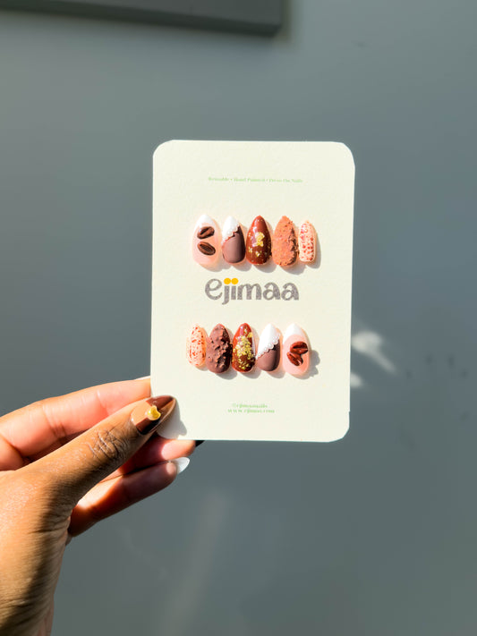 Hand holding a card with press on nails labeled 'ejimaa' against a plain background