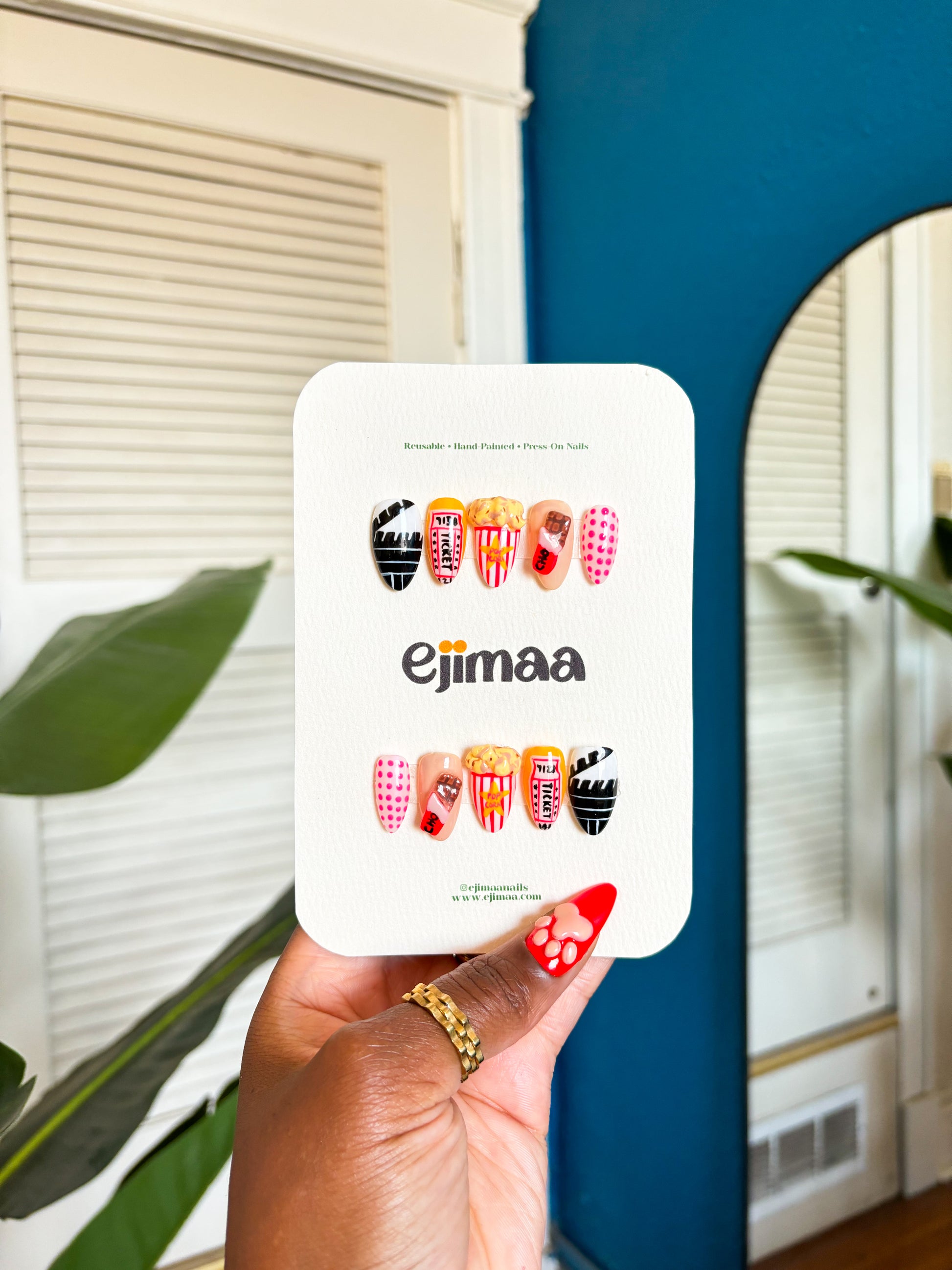 Hand holding a cinema/movie theater set with, chocolate bar, popcorn, movie ticket and polka dots on an ejimaa nail branded card. 