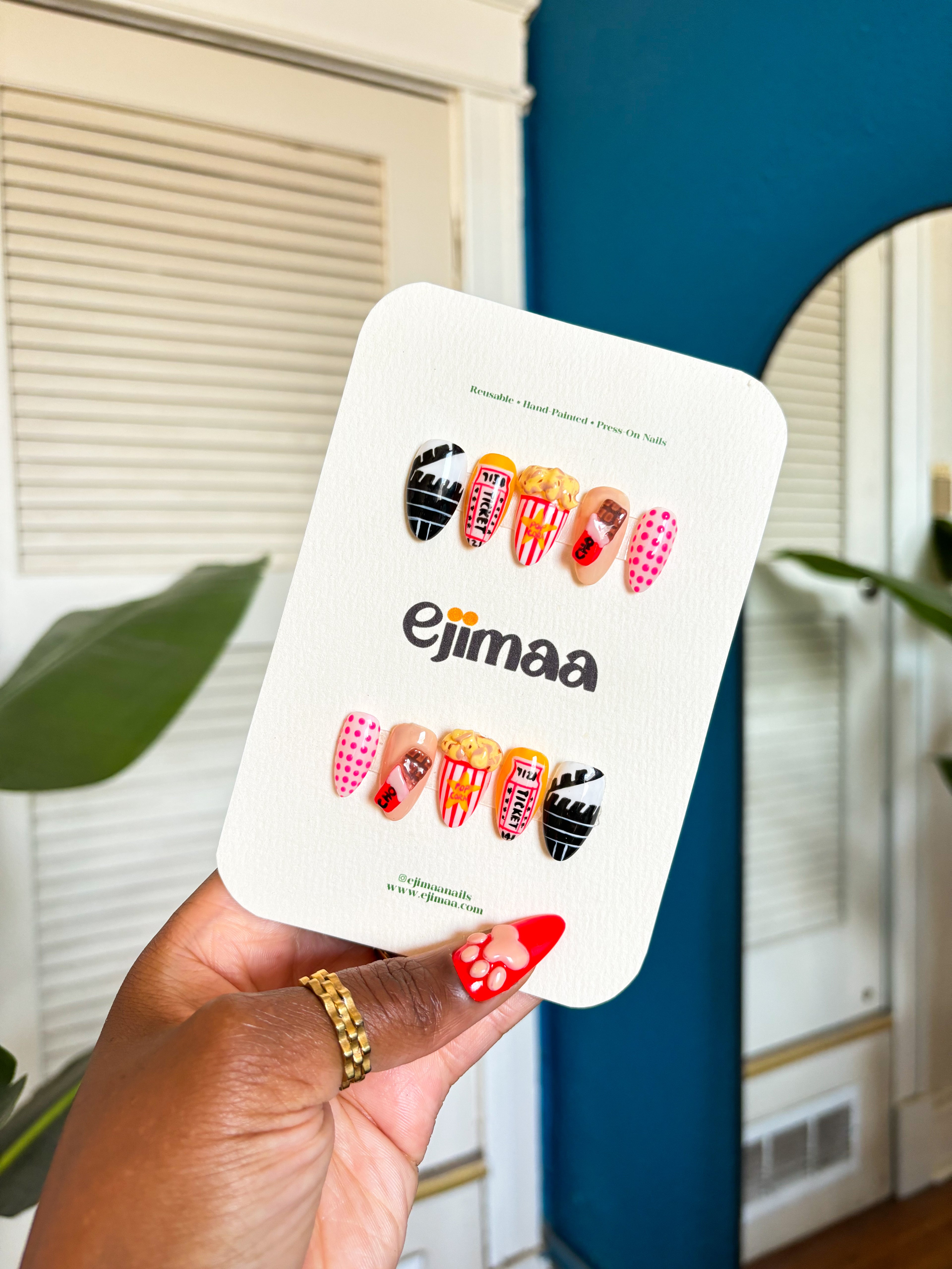 Hand holding a cinema/movie theater set with, chocolate bar, popcorn, movie ticket and polka dots on an ejimaa nail branded card. 